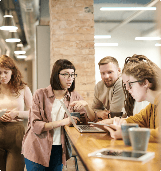 A group of people sitting at a table in front of a laptop and talking