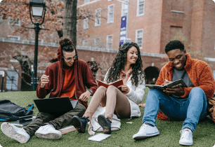 A group of students sitting on the grass looking at a laptop and reading.