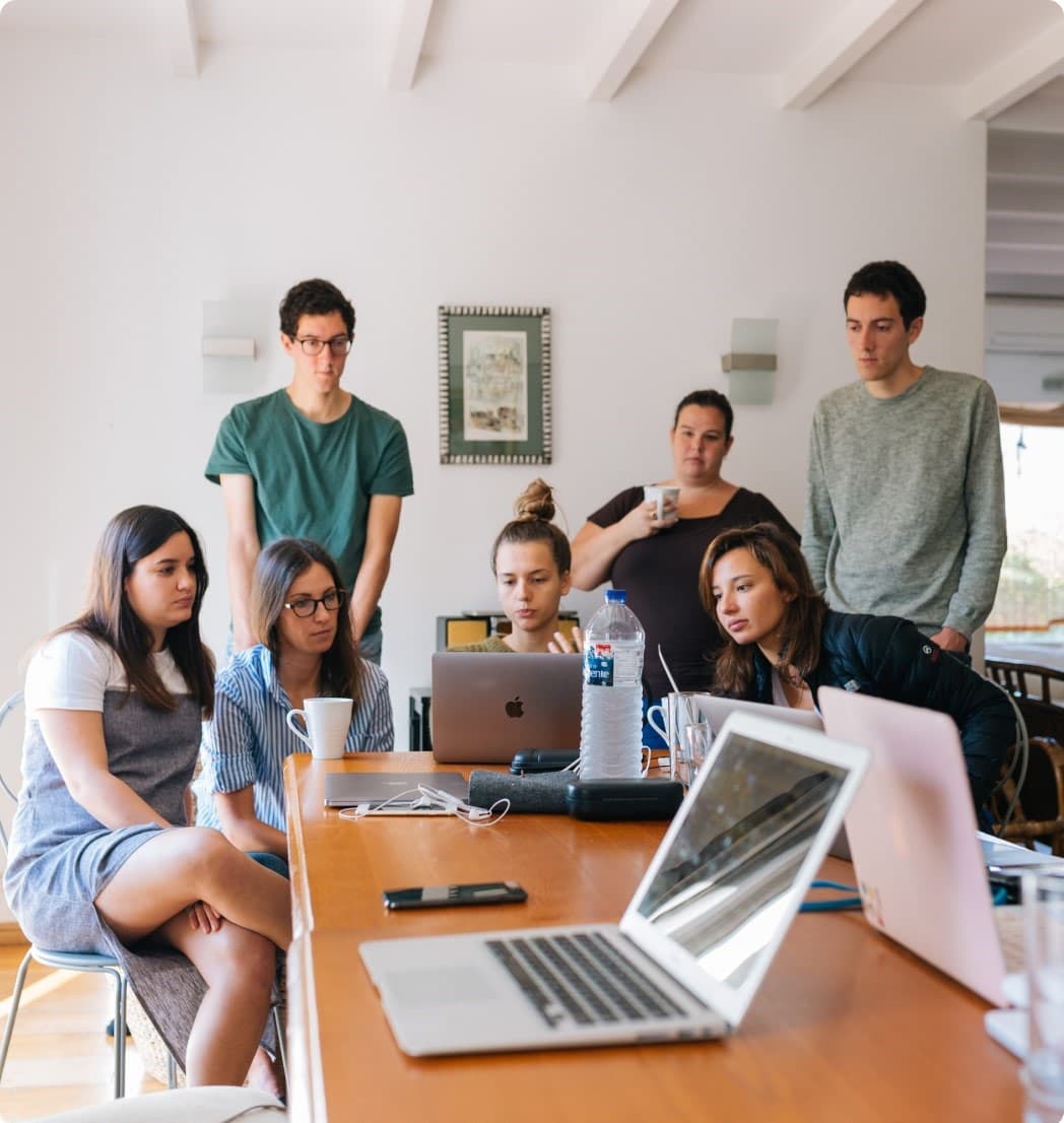 A group of people sitting around a table with laptops